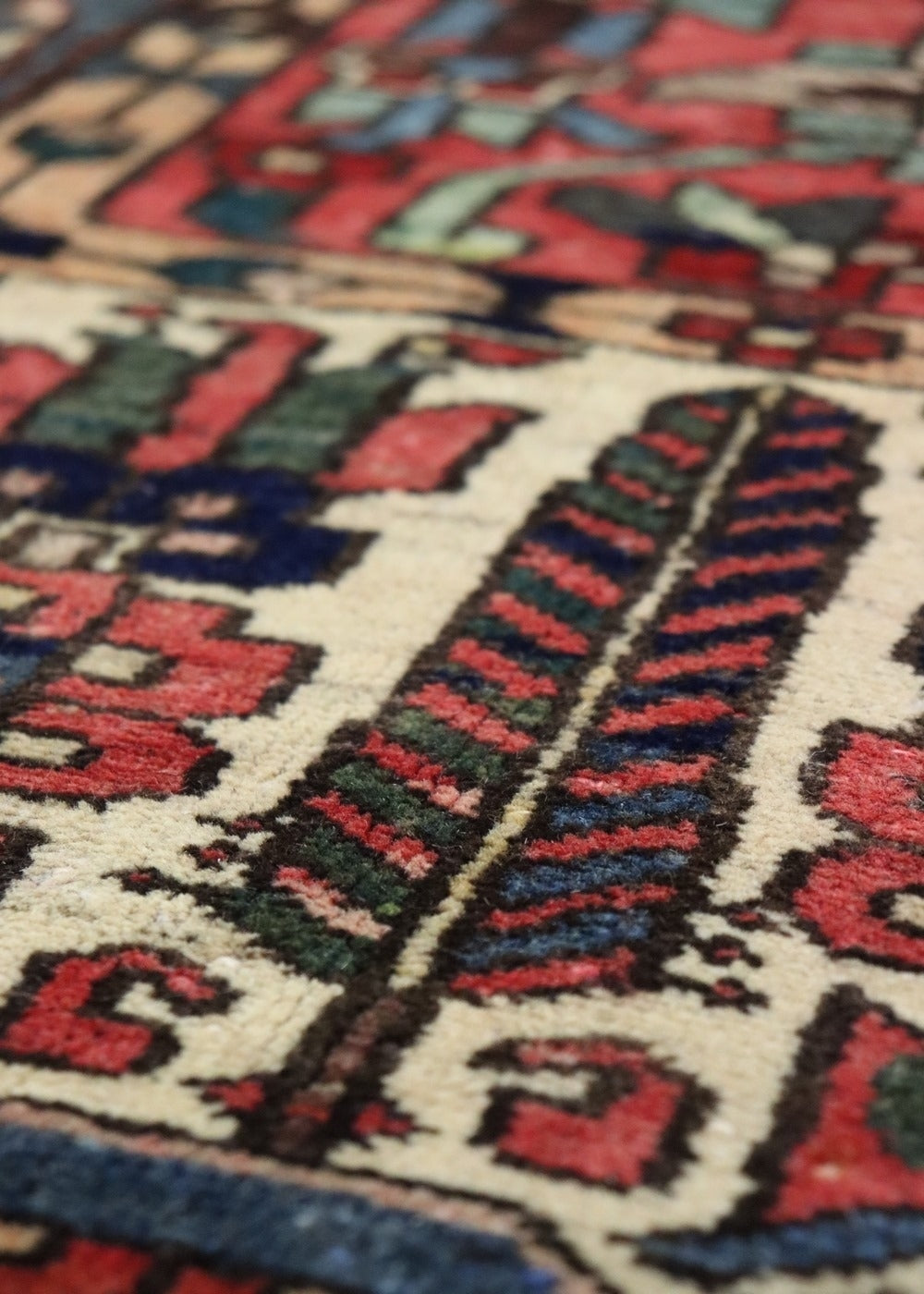 Close-up of handwoven rug detail, showcasing rich reds, blues, and greens in a tribal design.
