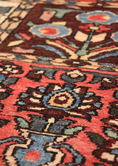 Close-up of antique rug detail; vibrant red, blue, and brown floral pattern, handwoven texture.
