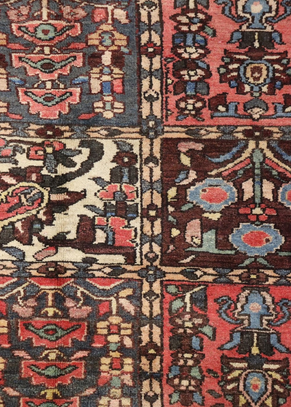 Detailed close-up of antique rug's handwoven tribal design, showcasing rich reds, blues, and creams.
