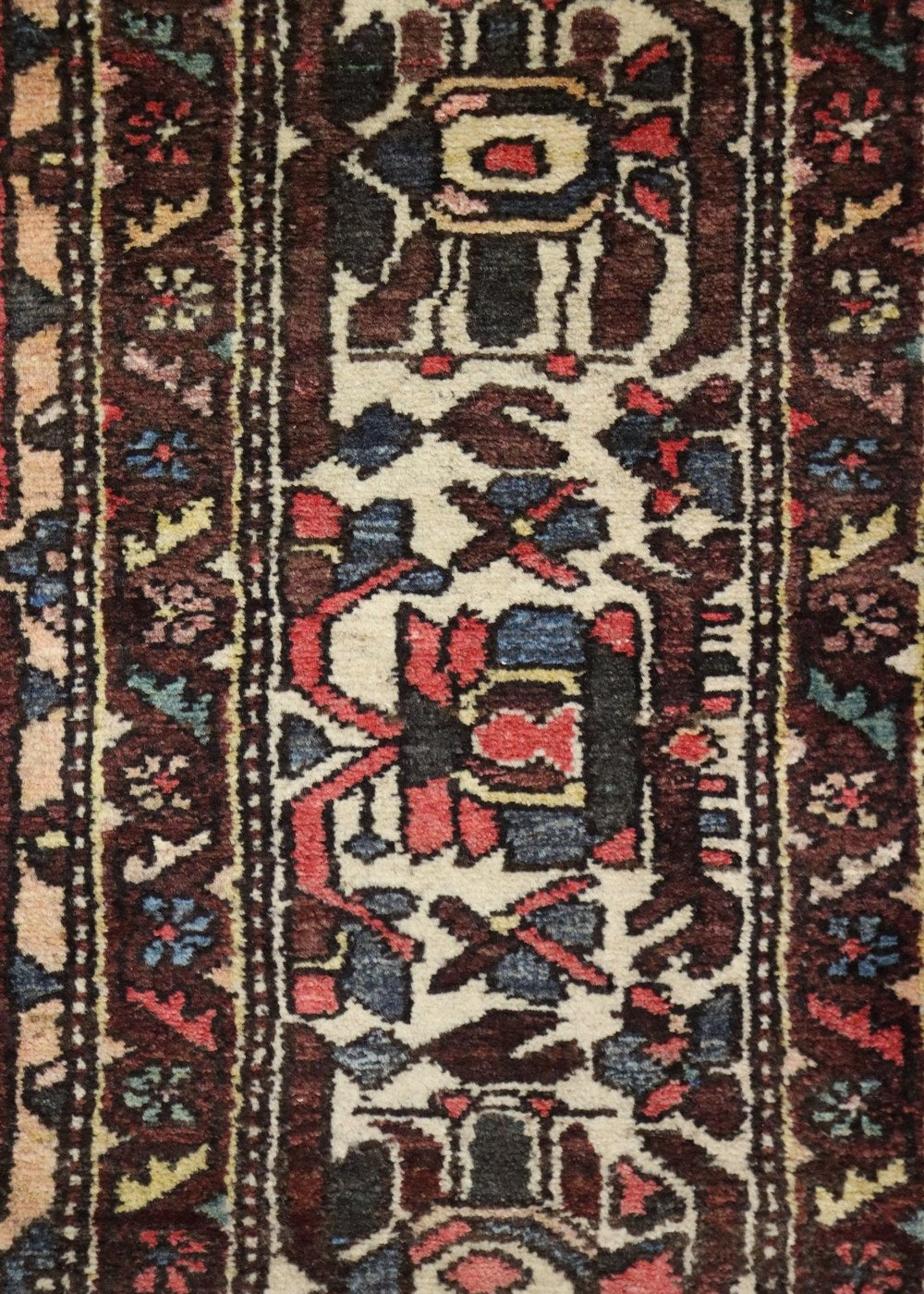 Close-up of antique Bakhtiari rug detail, showcasing intricate handwoven floral and geometric patterns in deep reds, blues, and creams.
