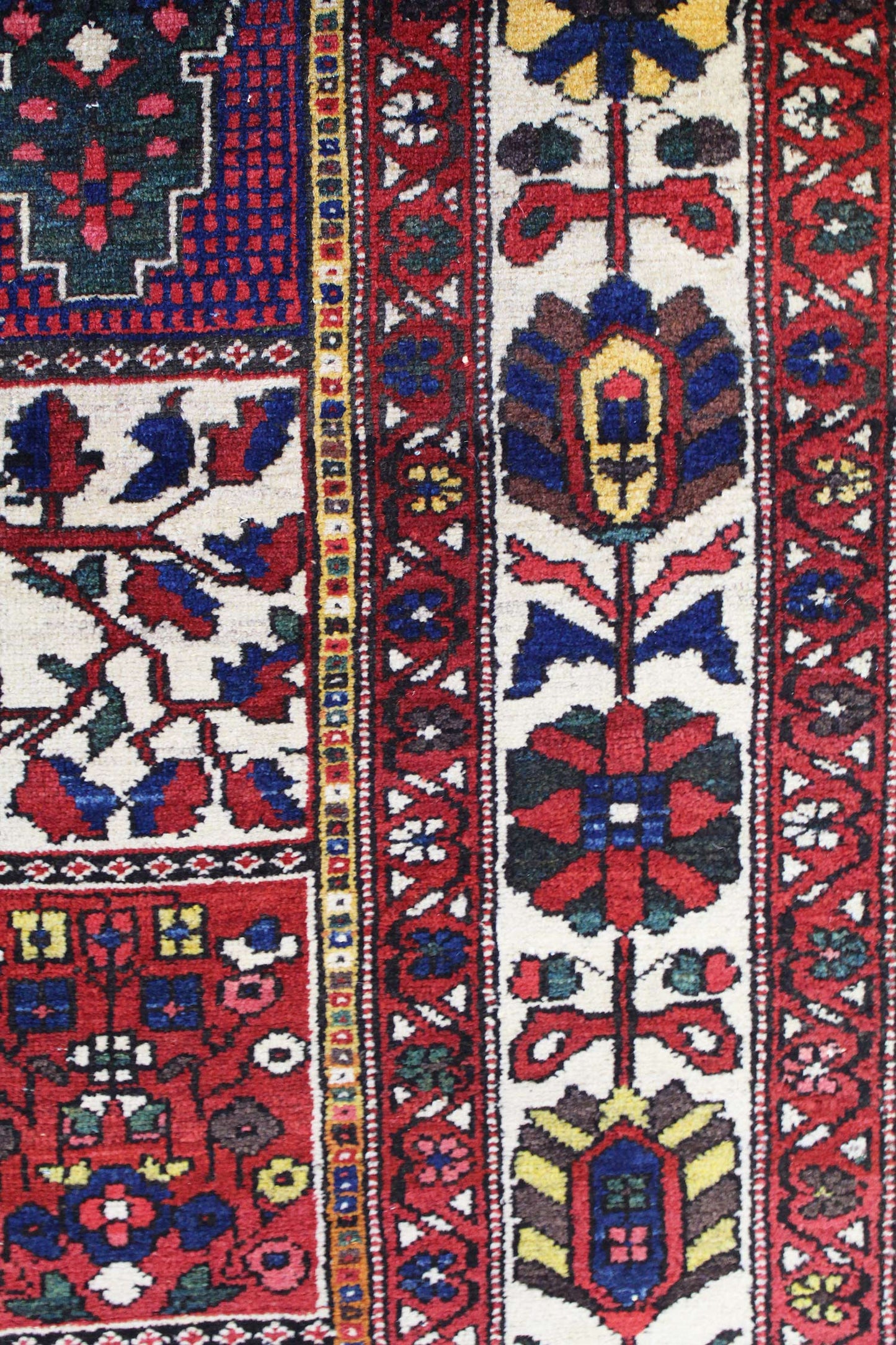 Detail of antique Bakhtiari rug, showcasing vibrant red, blue, and ivory floral patterns.
