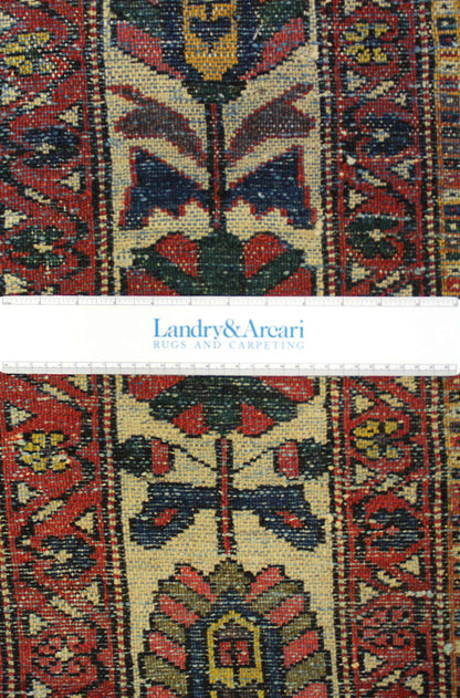 Close-up detail of antique tribal rug's handwoven floral pattern, showcasing rich reds and blues.
