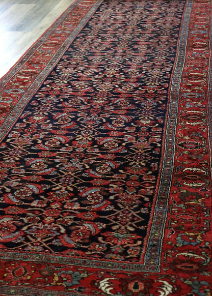 Handwoven antique Bijar rug, detailed floral pattern in rich reds and blues, shown on hardwood floor.
