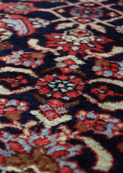 Close-up of a richly colored antique rug, showcasing intricate handwoven details in red, blue, and beige.
