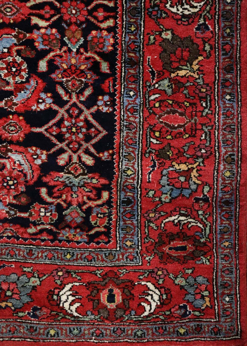 Detail of antique Bijar rug's handwoven border, showcasing red and navy floral patterns.
