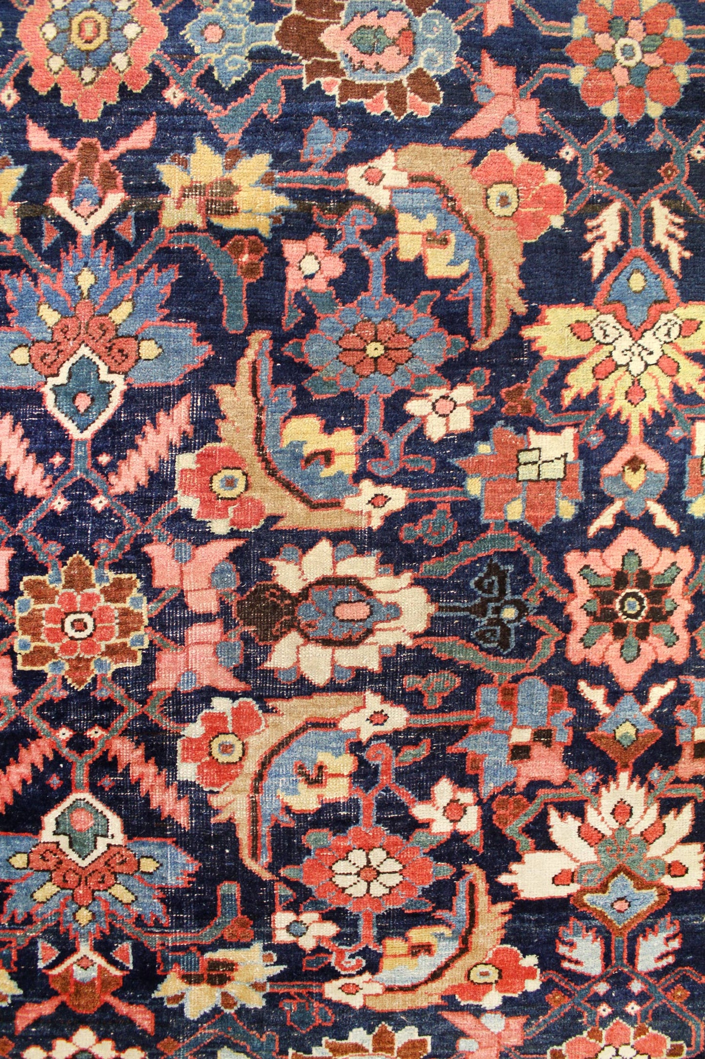 Detailed close-up of a vintage handwoven rug showcasing a rich navy blue background with intricate floral and arabesque patterns in red, pink, and beige.
