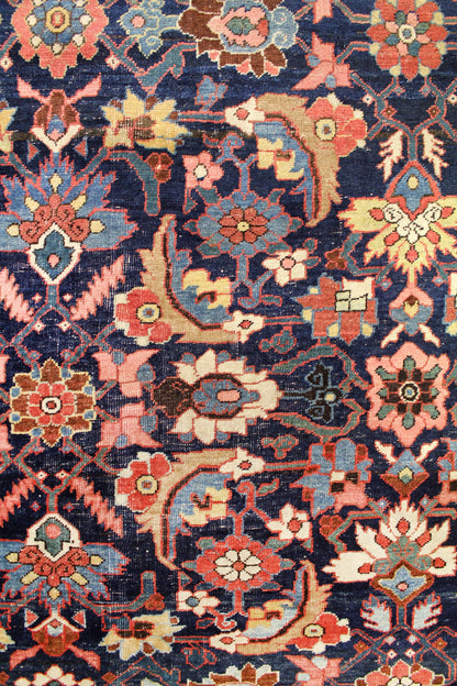 Detailed close-up of a vintage handwoven rug showcasing a rich navy blue background with intricate floral and arabesque patterns in red, pink, and beige.
