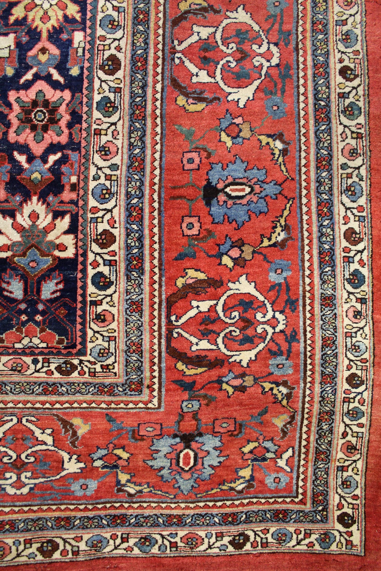Detail of antique Bijar rug's border, showcasing intricate floral and geometric patterns in red, blue, and cream wool.

