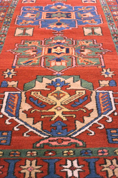 Handwoven Heriz rug detail, vibrant red base with intricate blue, green, and beige tribal patterns.

