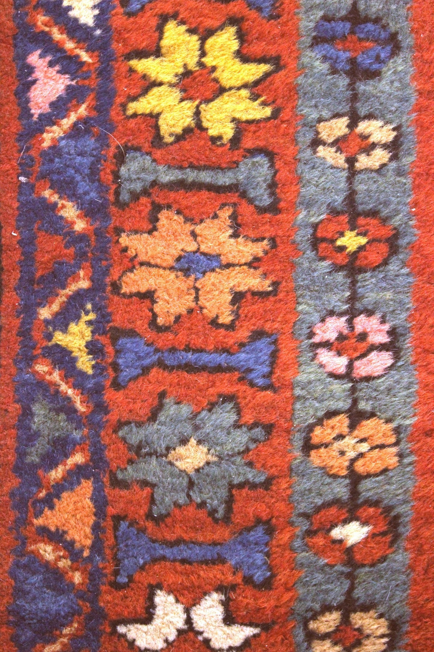 Close-up of antique Heriz rug detail: vibrant floral pattern in red, blue, and yellow wool.
