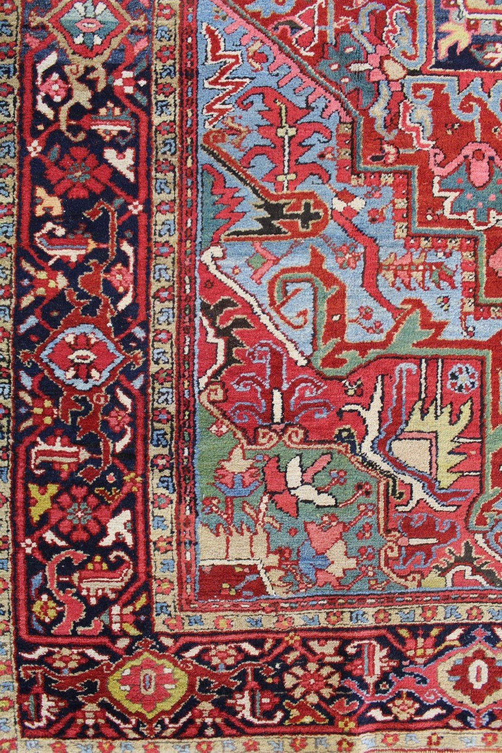 Antique Heriz rug detail: vibrant red, blue, and beige patterns, intricate tribal design.
