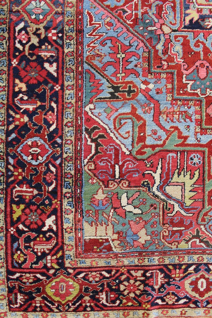 Antique Heriz rug detail: vibrant red, blue, and beige patterns, intricate tribal design.
