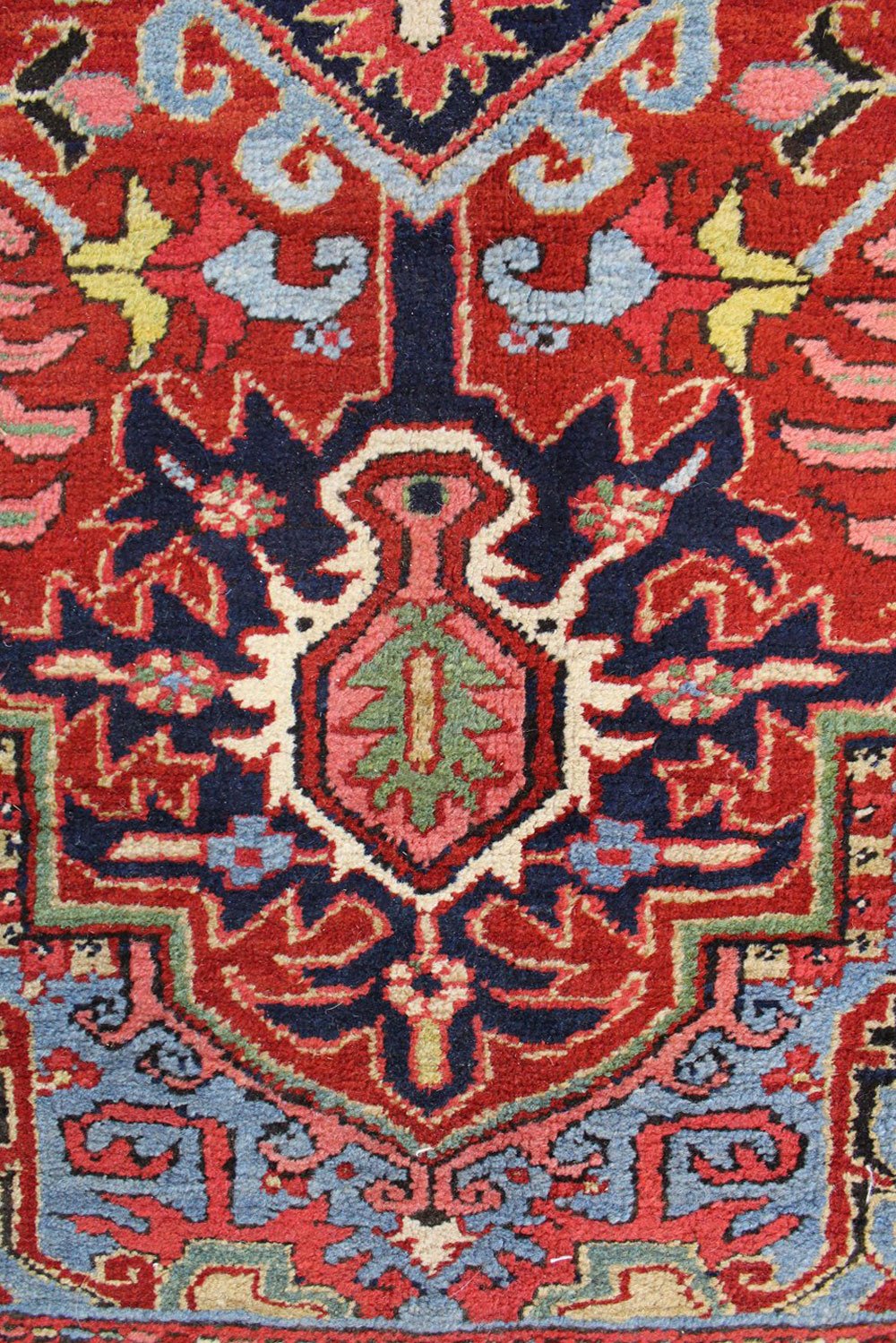 Close-up detail of an antique Heriz rug, showcasing its intricate red, blue, and ivory floral pattern.
