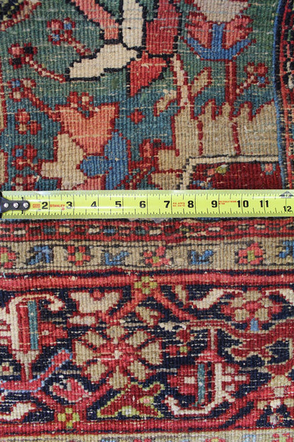 Close-up of antique Heriz rug detail, showing intricate floral pattern in red, blue, and beige, measured with tape.
