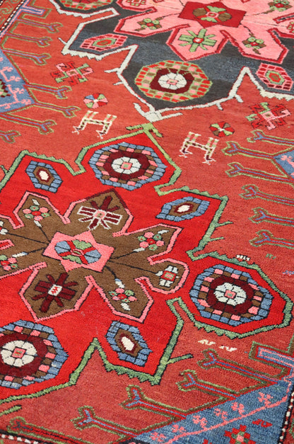 Detail of antique handwoven rug with red background, intricate multicolored geometric patterns.
