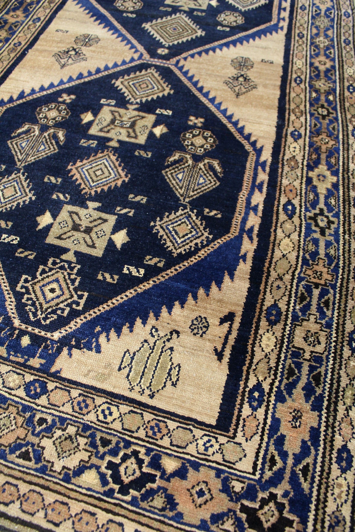 Handwoven tribal rug detail: intricate navy and beige geometric patterns, antique Malayer design.

