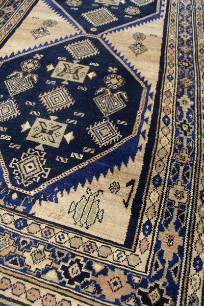 Handwoven tribal rug detail: intricate navy and beige geometric patterns, antique Malayer design.
