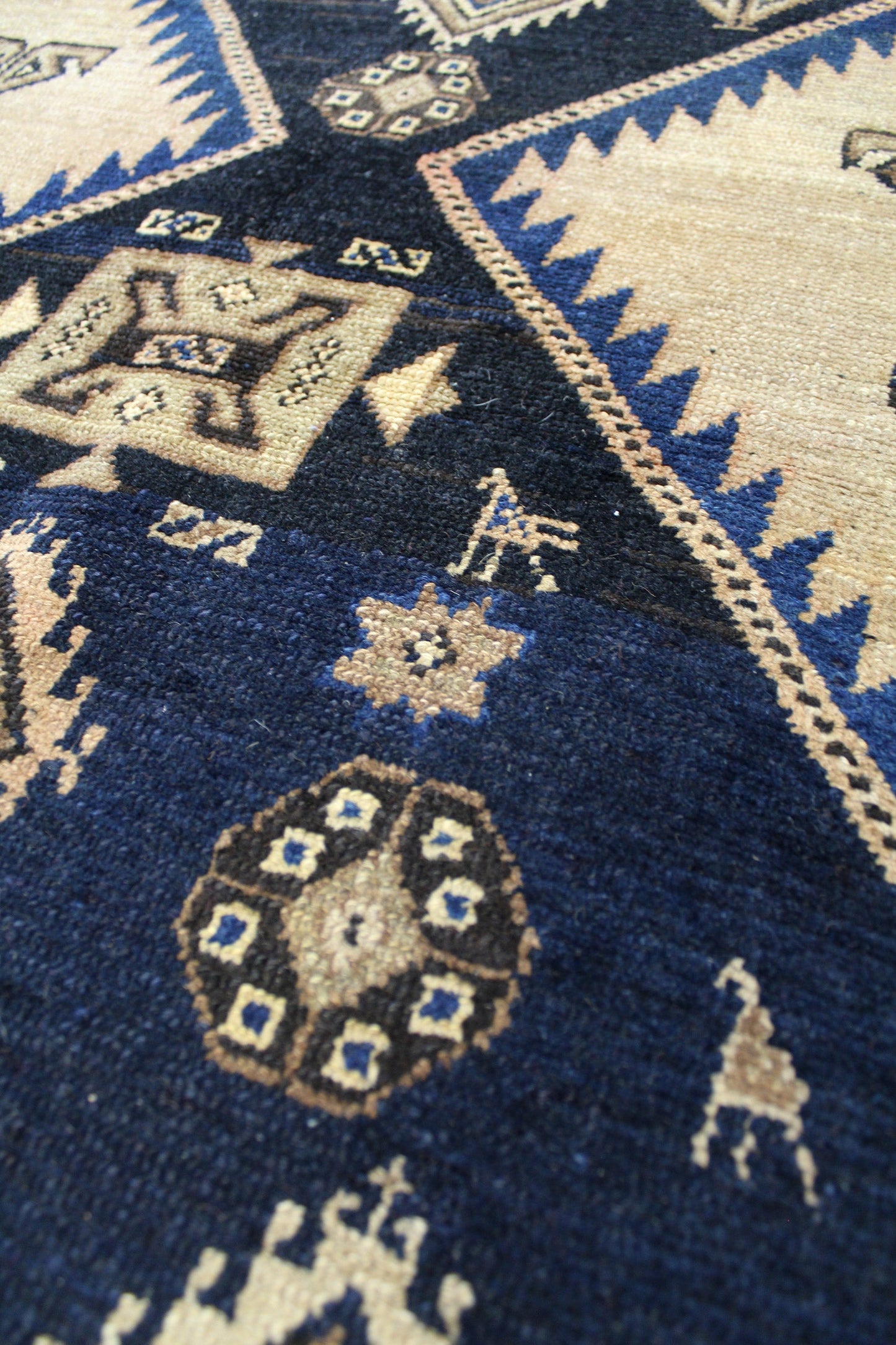 Detail of antique Malayer rug, showcasing handwoven tribal patterns in navy, beige, and black.
