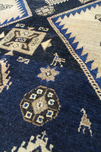 Detail of antique Malayer rug, showcasing handwoven tribal patterns in navy, beige, and black.
