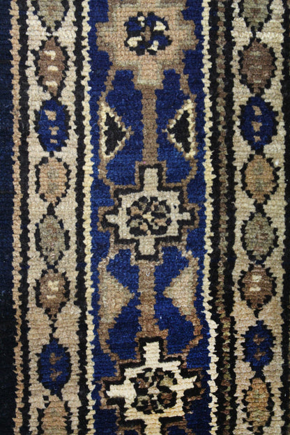 Close-up detail of antique rug's handwoven, tribal design; beige, brown, and navy blue patterns.
