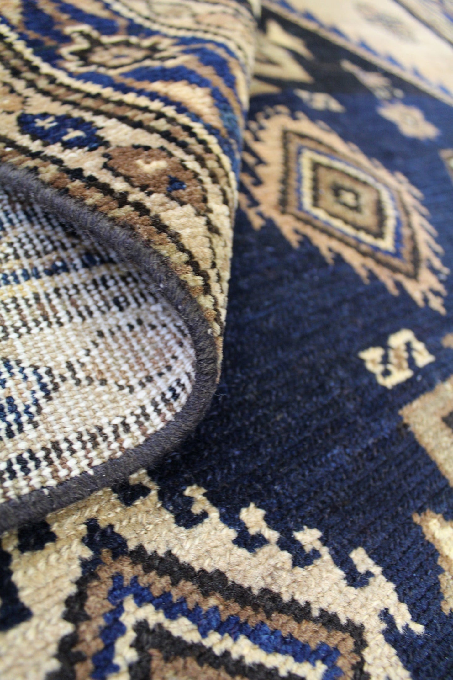 Close-up of handwoven rug detail, showcasing intricate tribal pattern in beige, navy, and brown.
