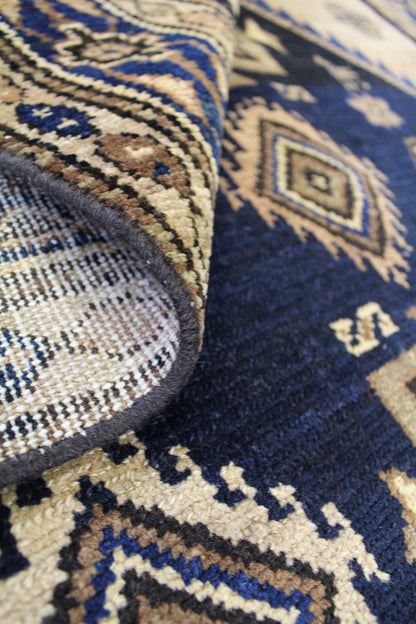 Close-up of handwoven rug detail, showcasing intricate tribal pattern in beige, navy, and brown.
