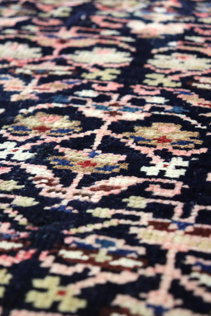 Close-up detail of a dark navy handwoven rug with a pink and cream floral pattern.
