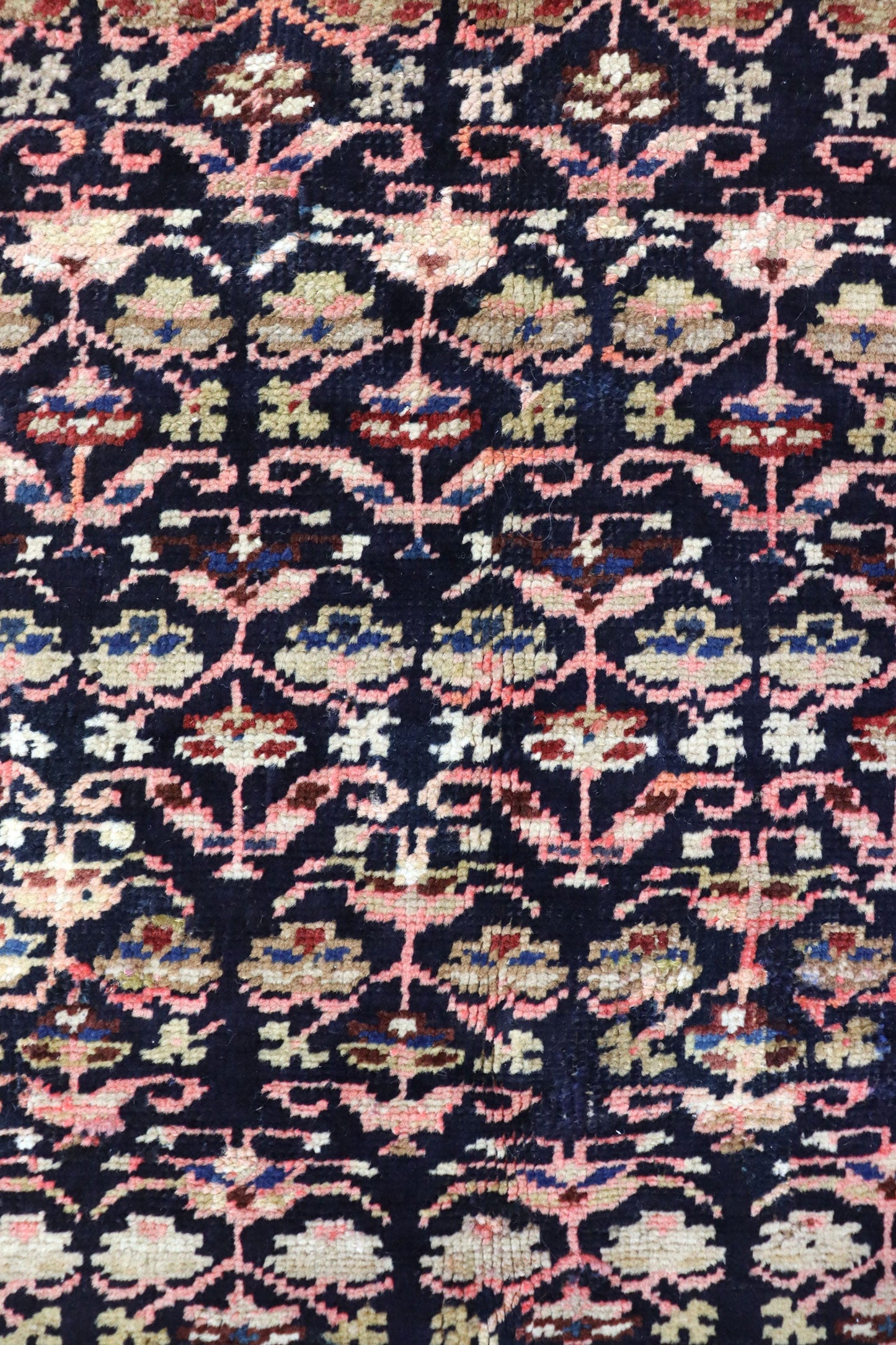 Close-up detail of antique Persian rug's handwoven floral pattern in dark navy, pink, and beige.
