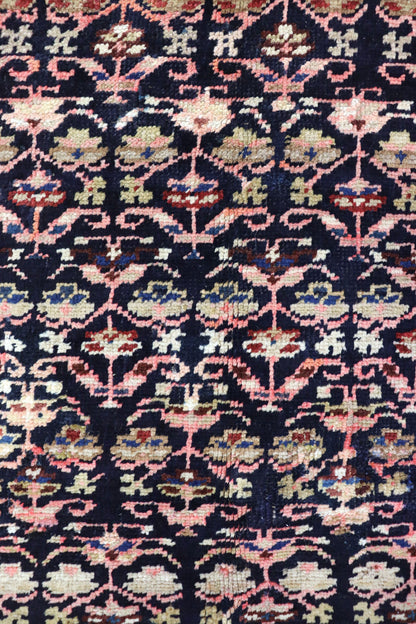 Close-up detail of antique Persian rug's handwoven floral pattern in dark navy, pink, and beige.
