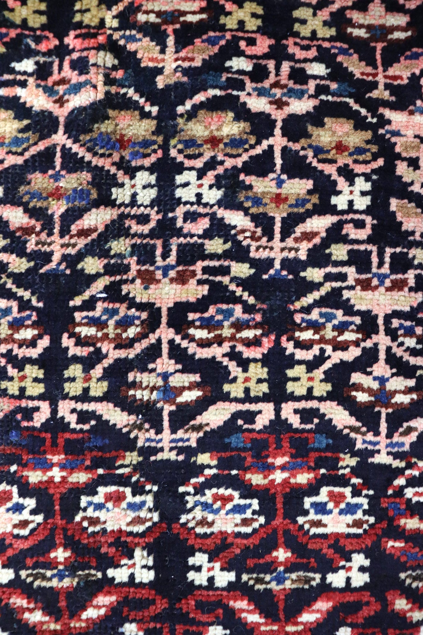 Close-up of antique handwoven rug displaying intricate, multicolored floral pattern on dark background.
