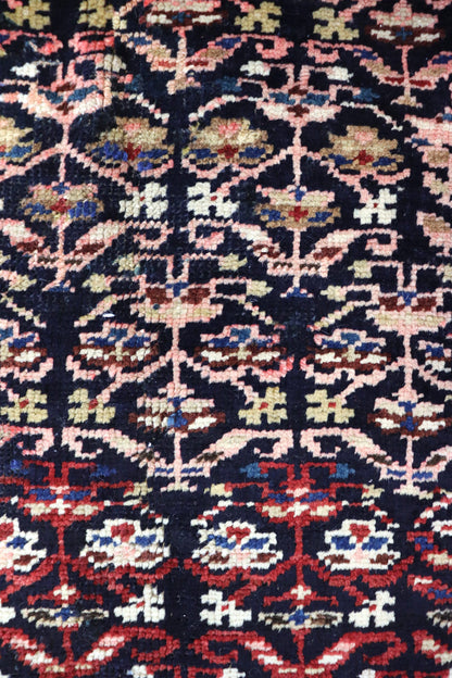 Close-up of antique handwoven rug displaying intricate, multicolored floral pattern on dark background.
