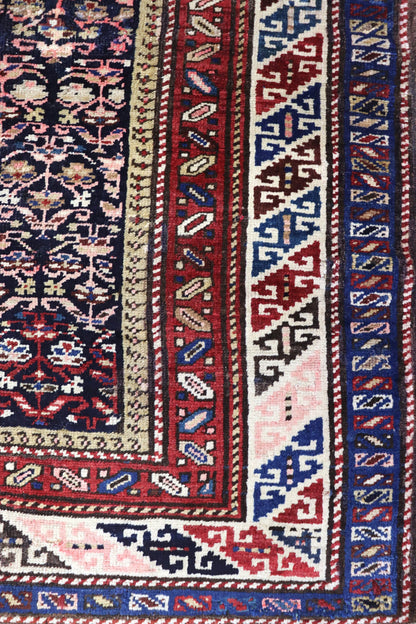 Detail of antique Persian rug's handwoven border, showcasing vibrant red, blue, and ivory patterns.

